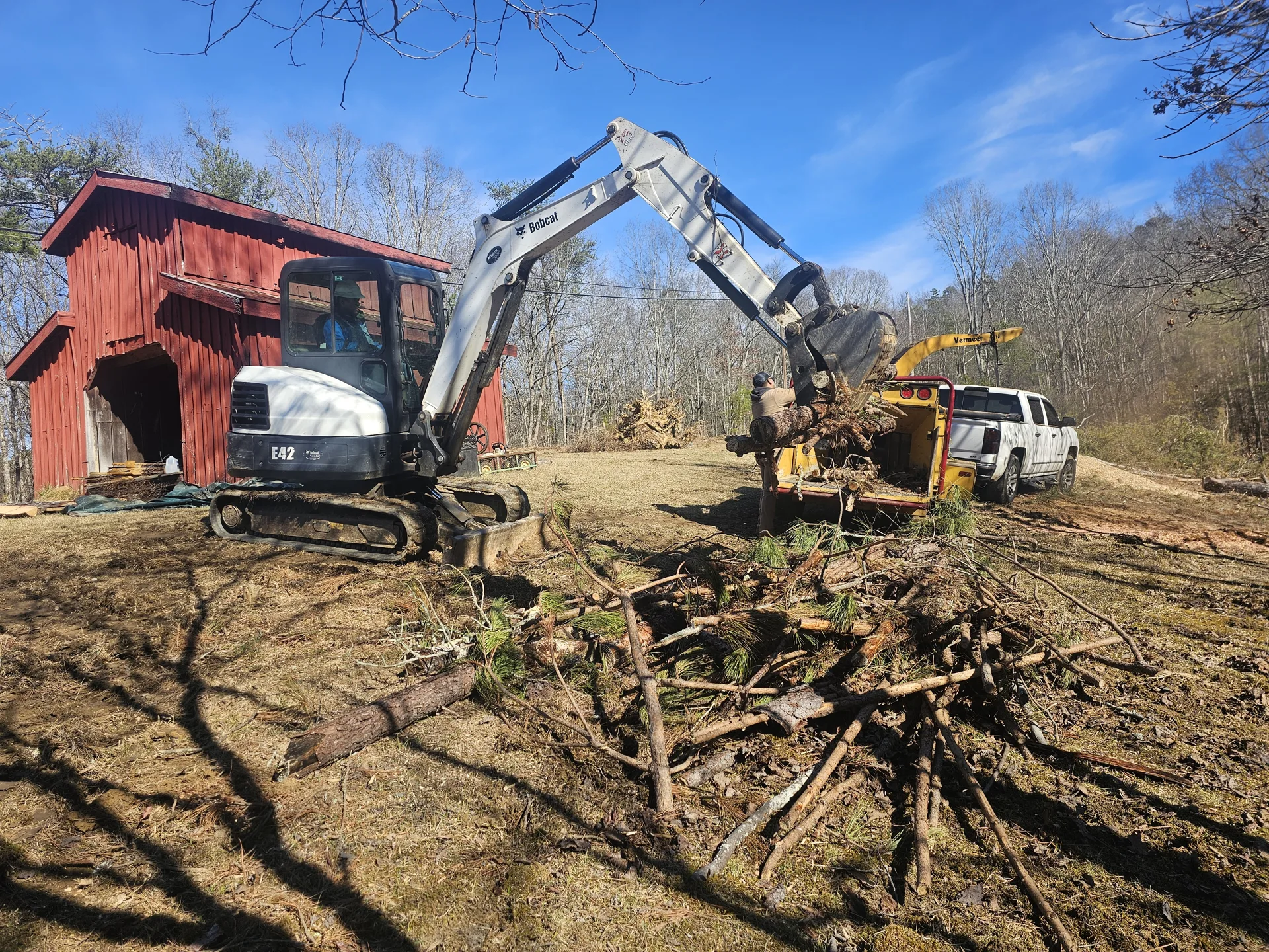 Excavator handling cut timber beside the wood chipper.