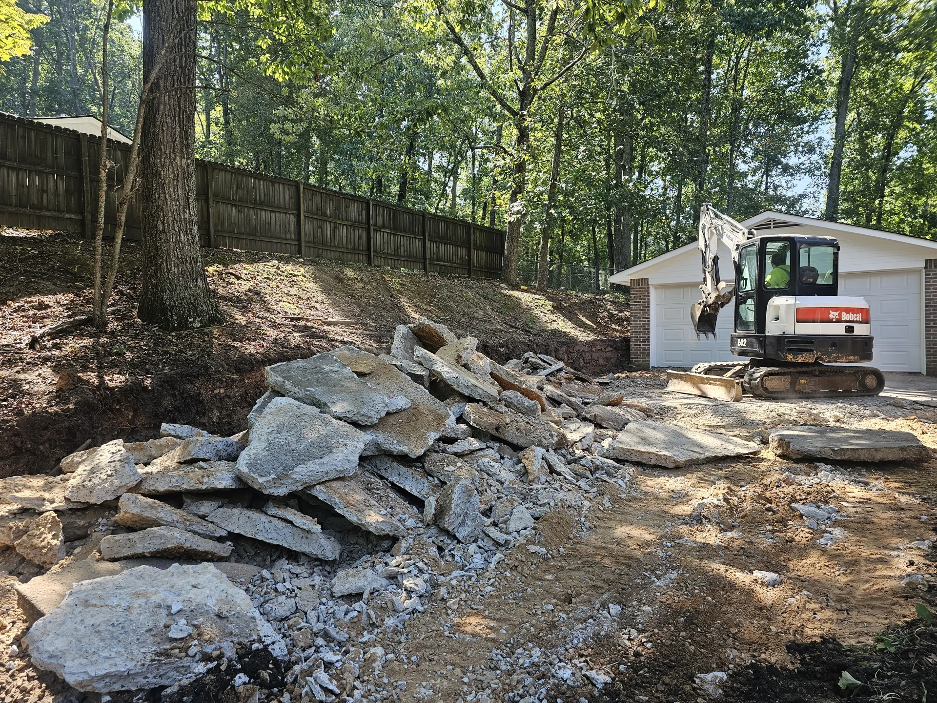 Excavator beside broken concrete ready for loading and removal.